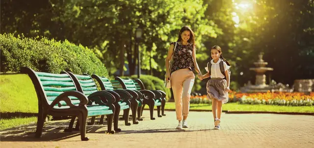 Mother and daughter walking through a park with benches and a fountain